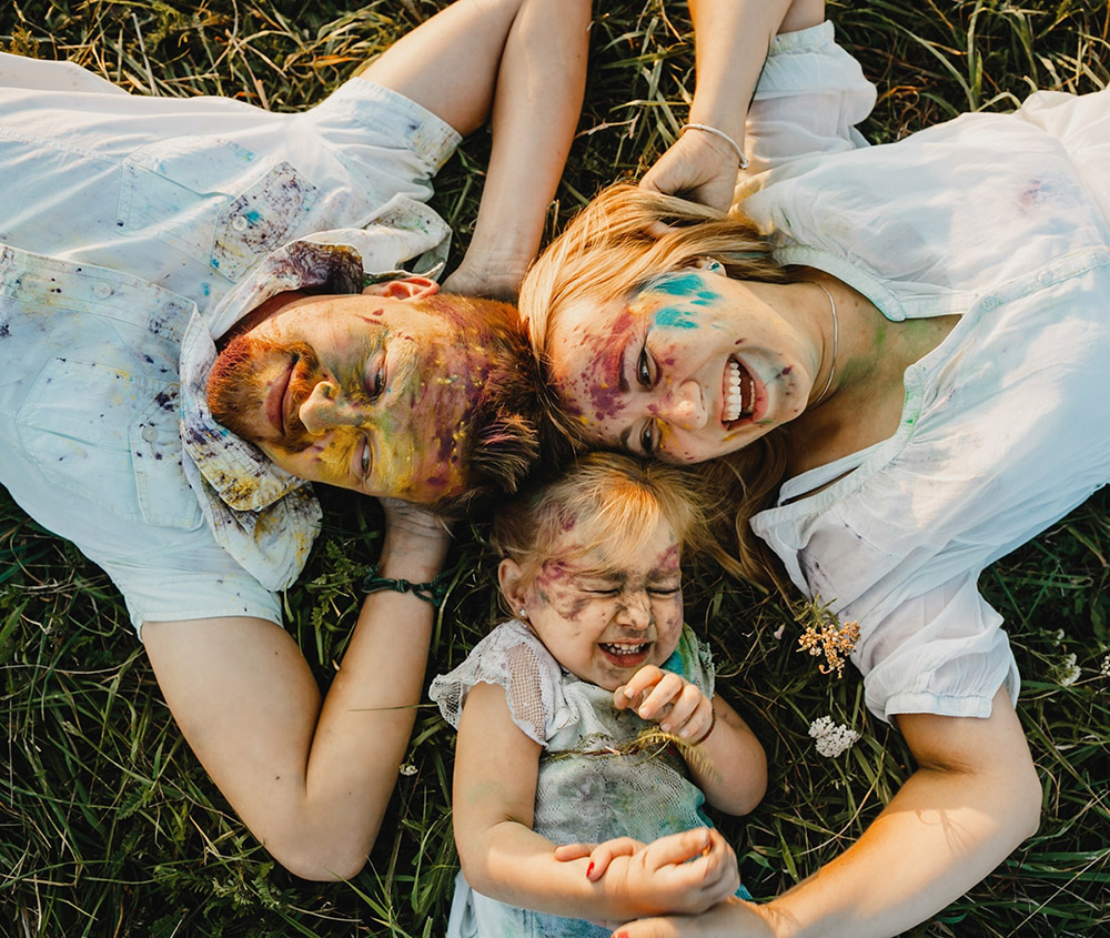 mom-dad-their-daughter-covered-with-colorful-paints-lie-green-lawn_8353-7534